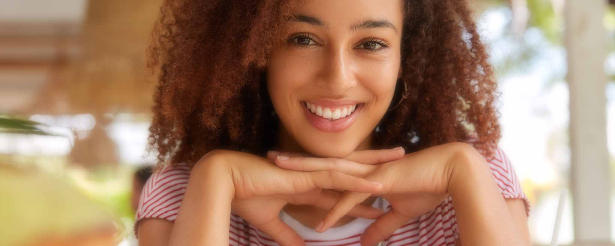 'A beautiful happy young curly-haired Black lady rests her head on her hands. (ai)'