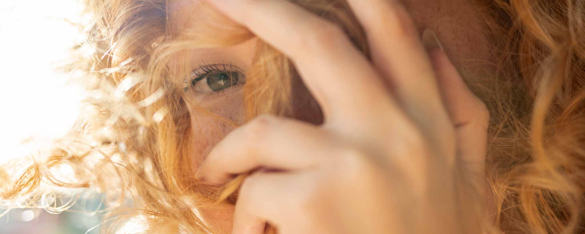'Redhead with curly hair shielding her eyes from the sunlight.'
