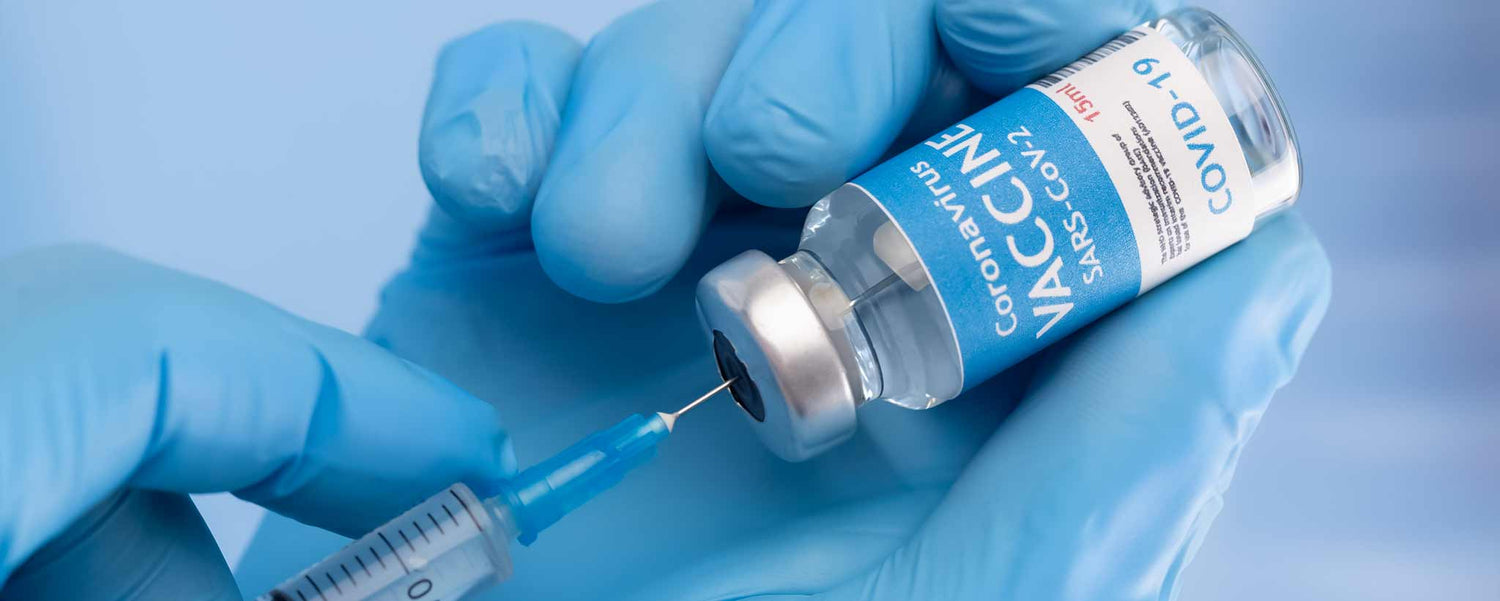Vaccine vial with syringe and gloved hands on a blue background.