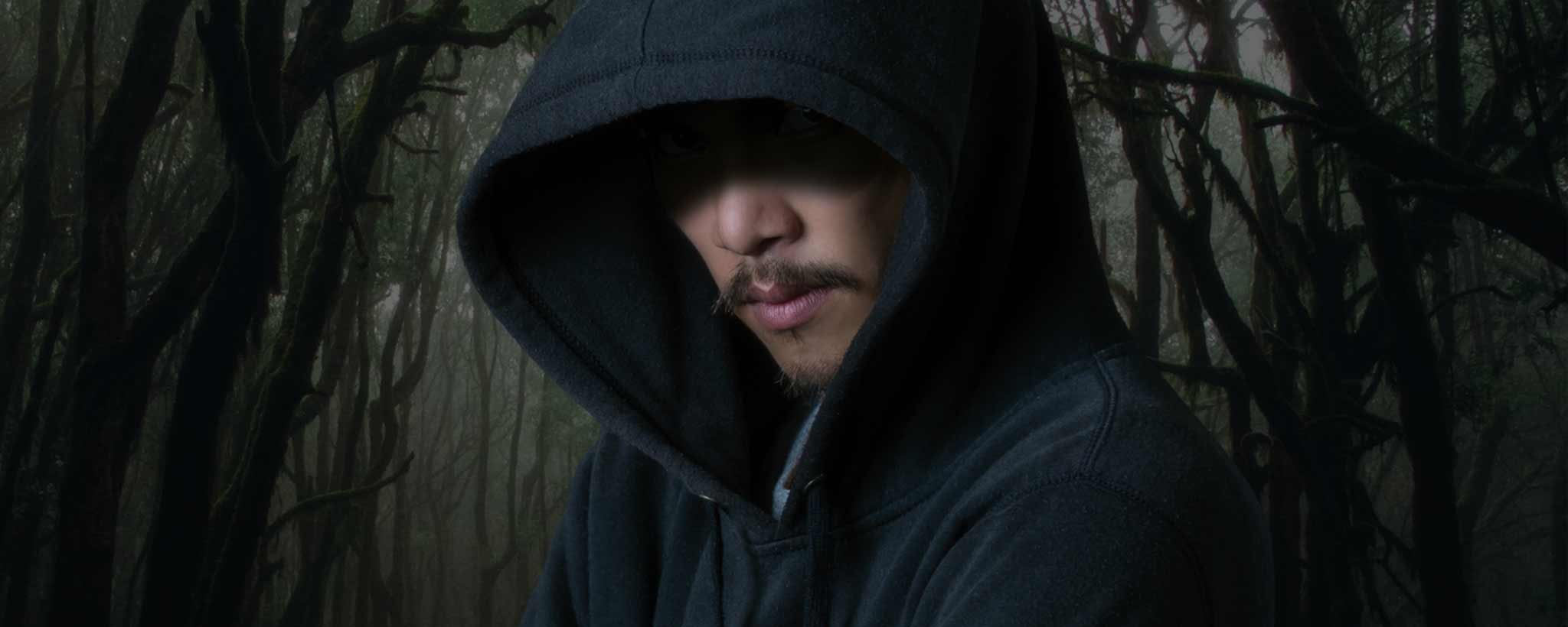 'A hooded man in the darkness with trees in the background.'