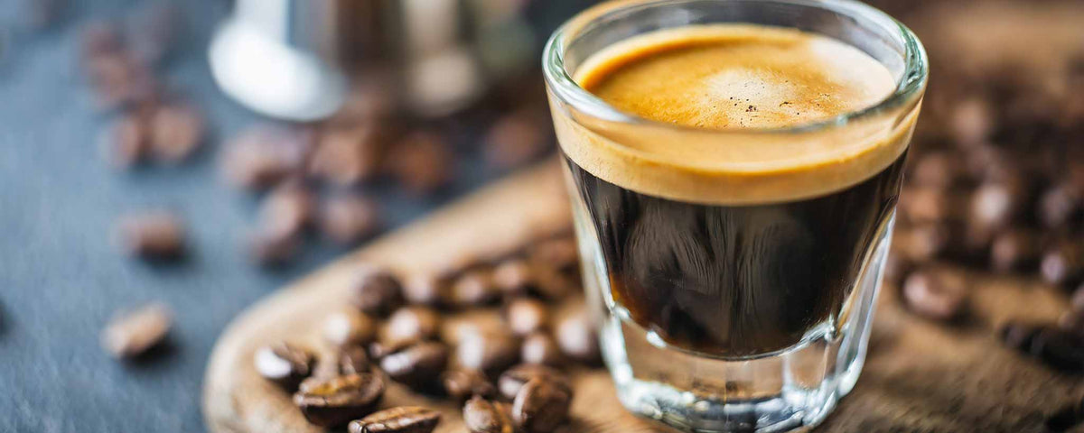 'Espresso shot in a glass with coffee beans on a wooden board.'