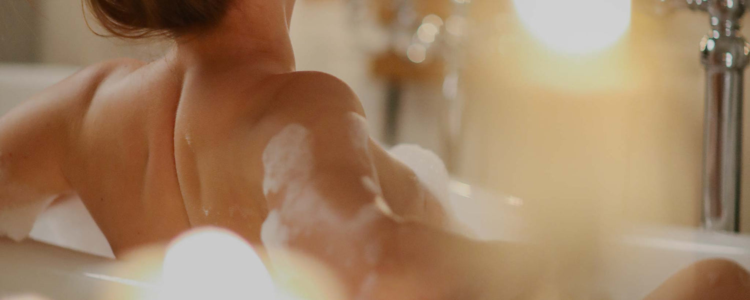 The shoulders and back of a female taking a bubble bath.