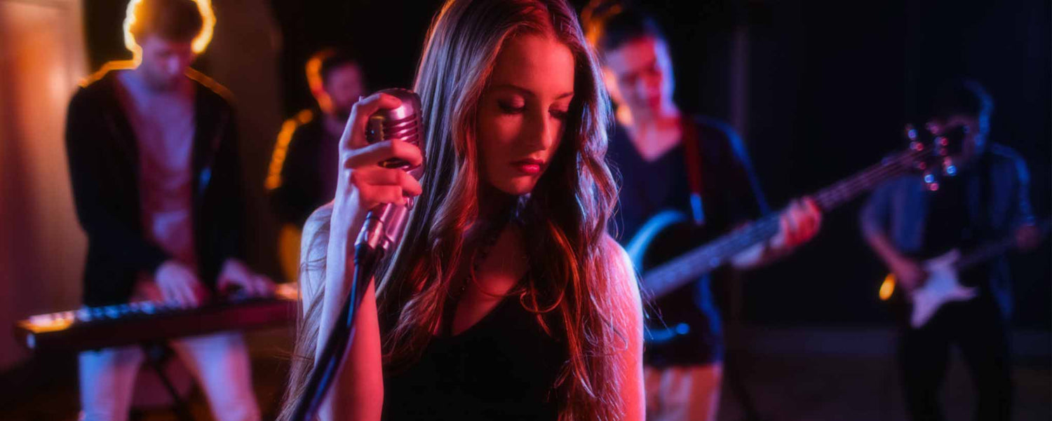A female singer performs under colorful lights with her band.