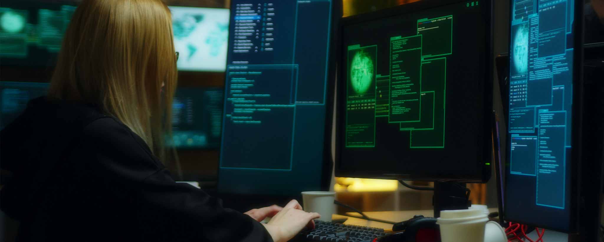 'A female hacker in front of several computer screens.'