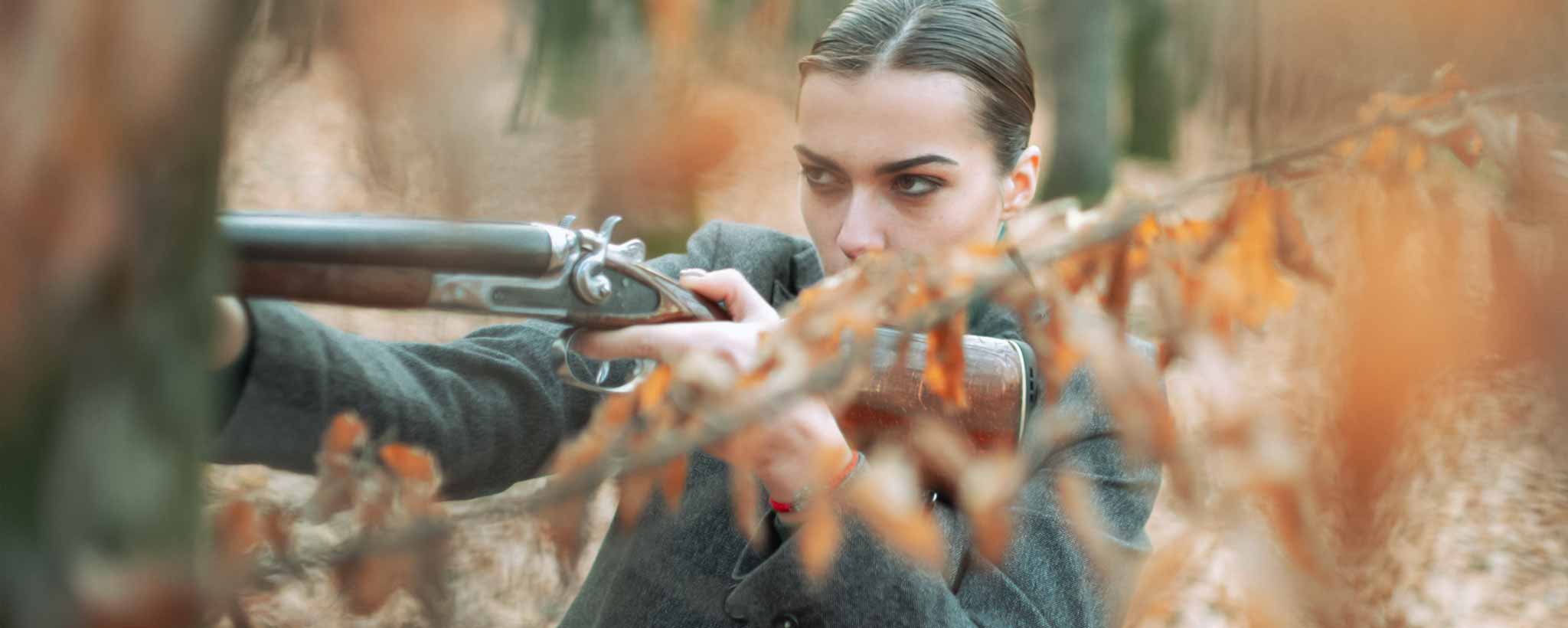 'A female aims a rifle in the forest.'