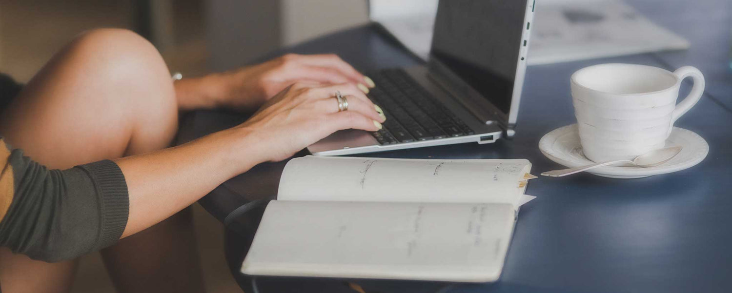 Woman typing on a a laptop computer with an open book.