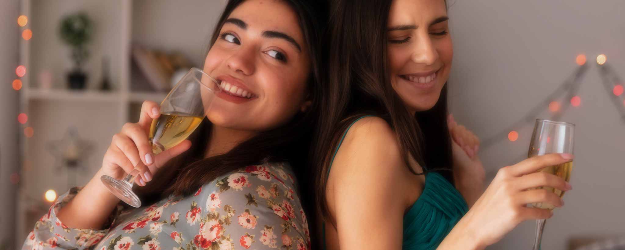 'Two back-to-back females with champagne glasses smile.'