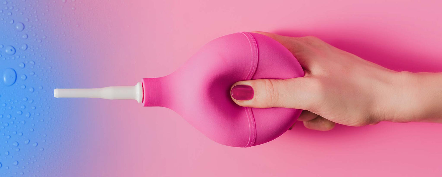 Female hand squeezing pink douche syringe.