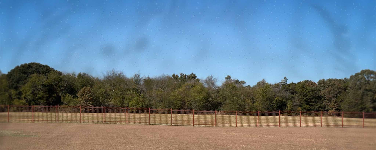 Open field with a fence and trees under a clear blue sky with floaters.