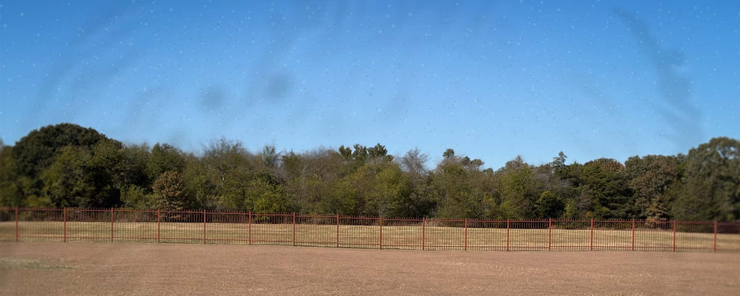 Open field with a fence and trees under a clear blue sky with floaters.