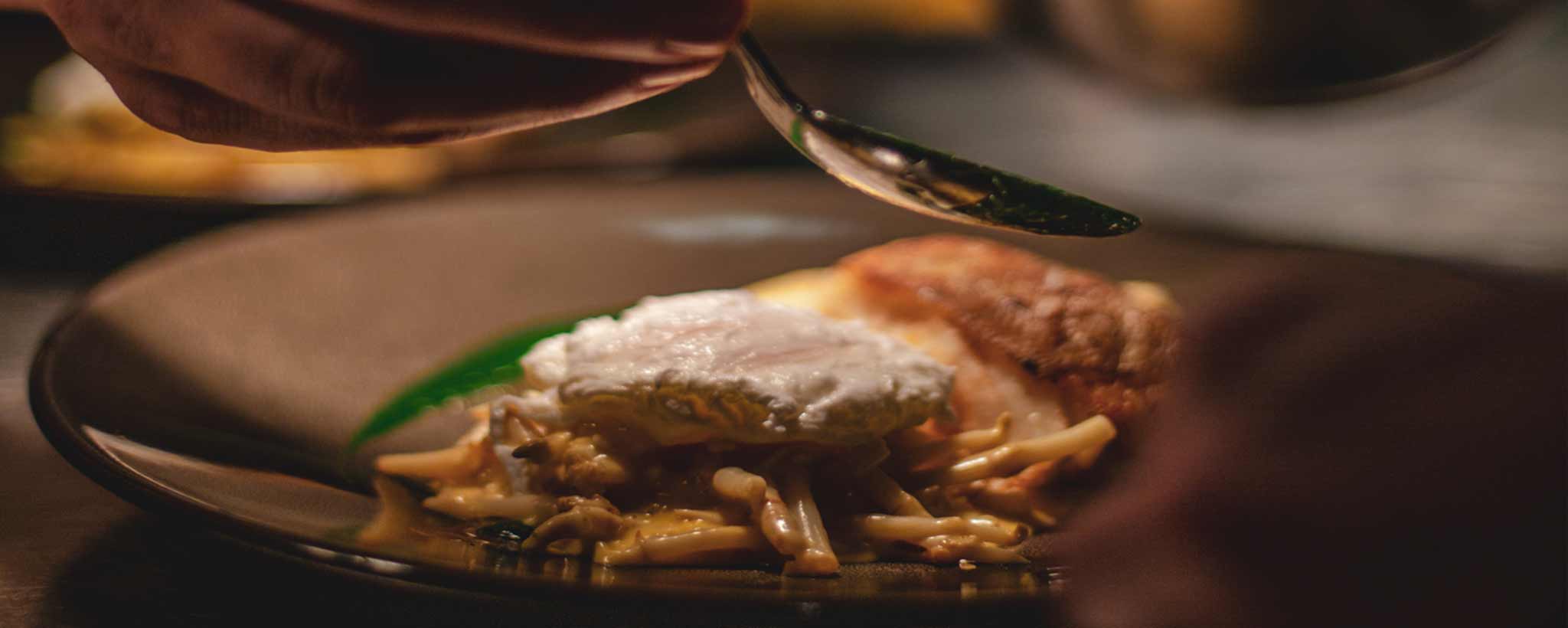 'Close-up of a plate with pasta and a poached egg, being drizzled with a sauce.'