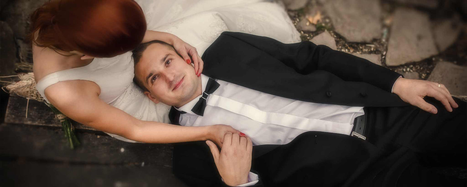 A redhead bride holds her groom's head, as he lies on her lap.