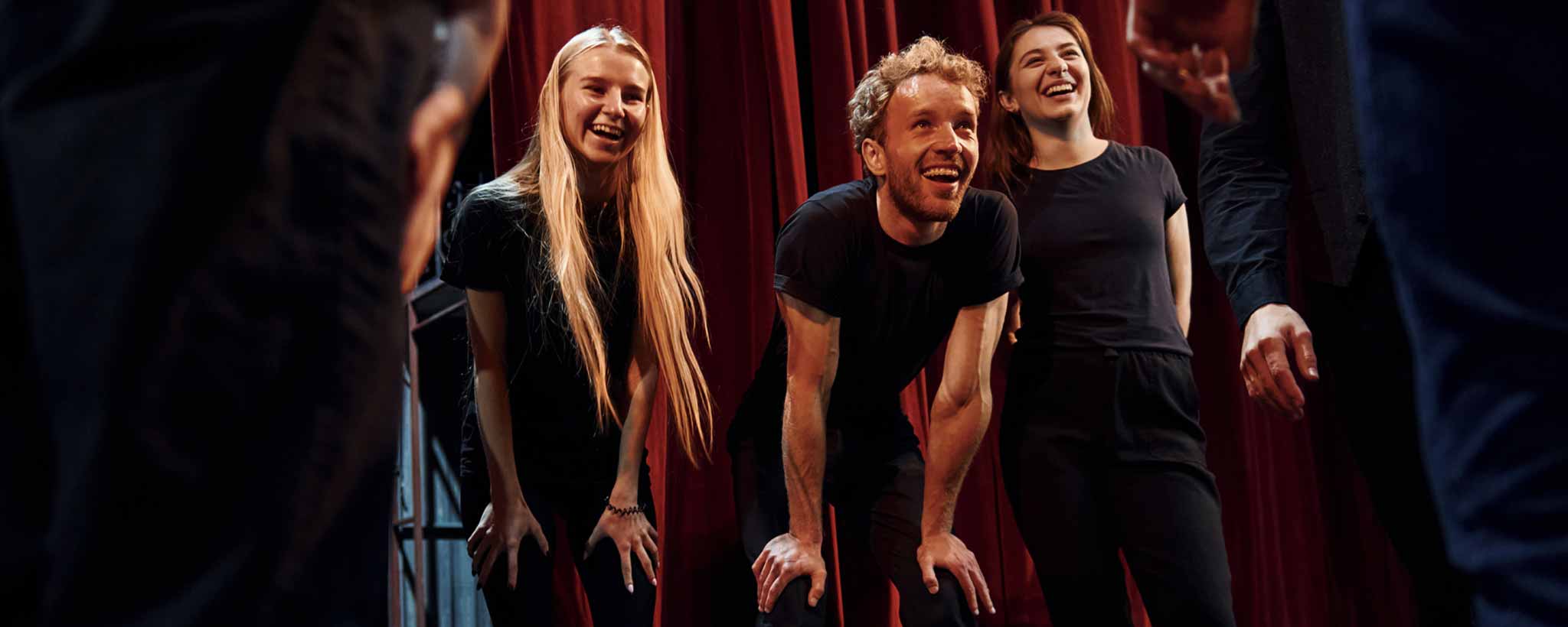 'Three actors smile behind the backstage red curtain.'