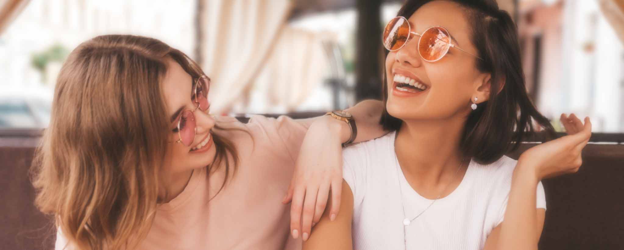 'A couple of White and Black young ladies smile and touch in a restaurant.'