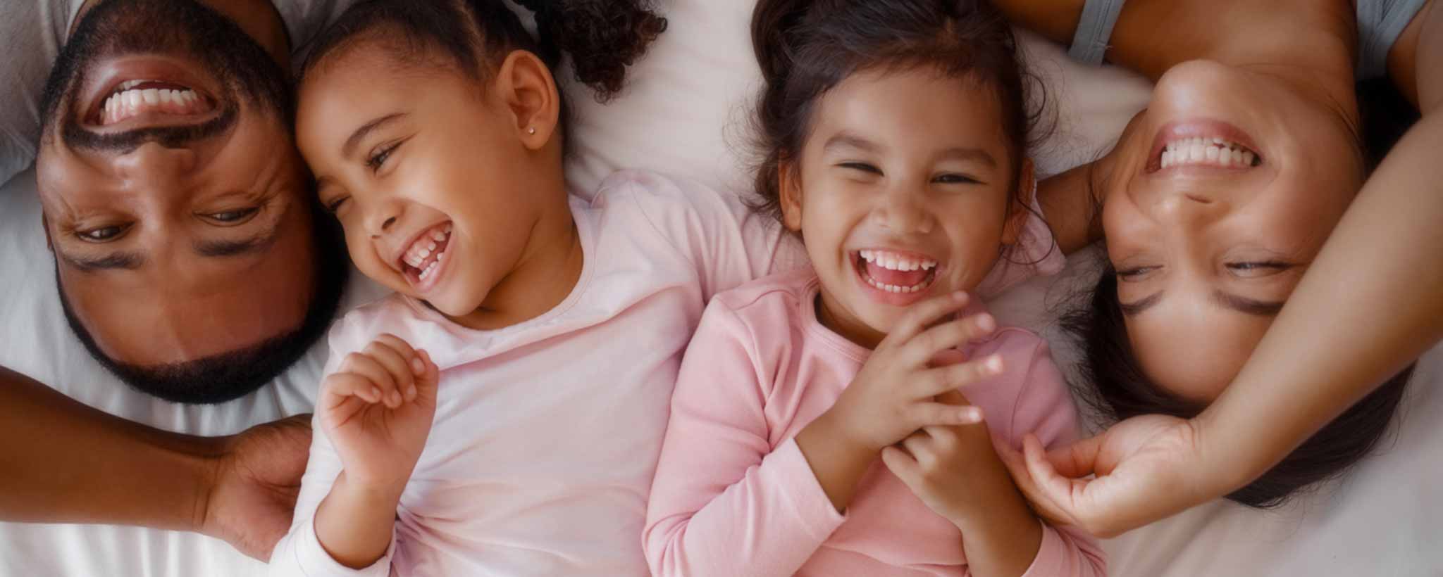 'Happy girls with their parents lie in bed.'