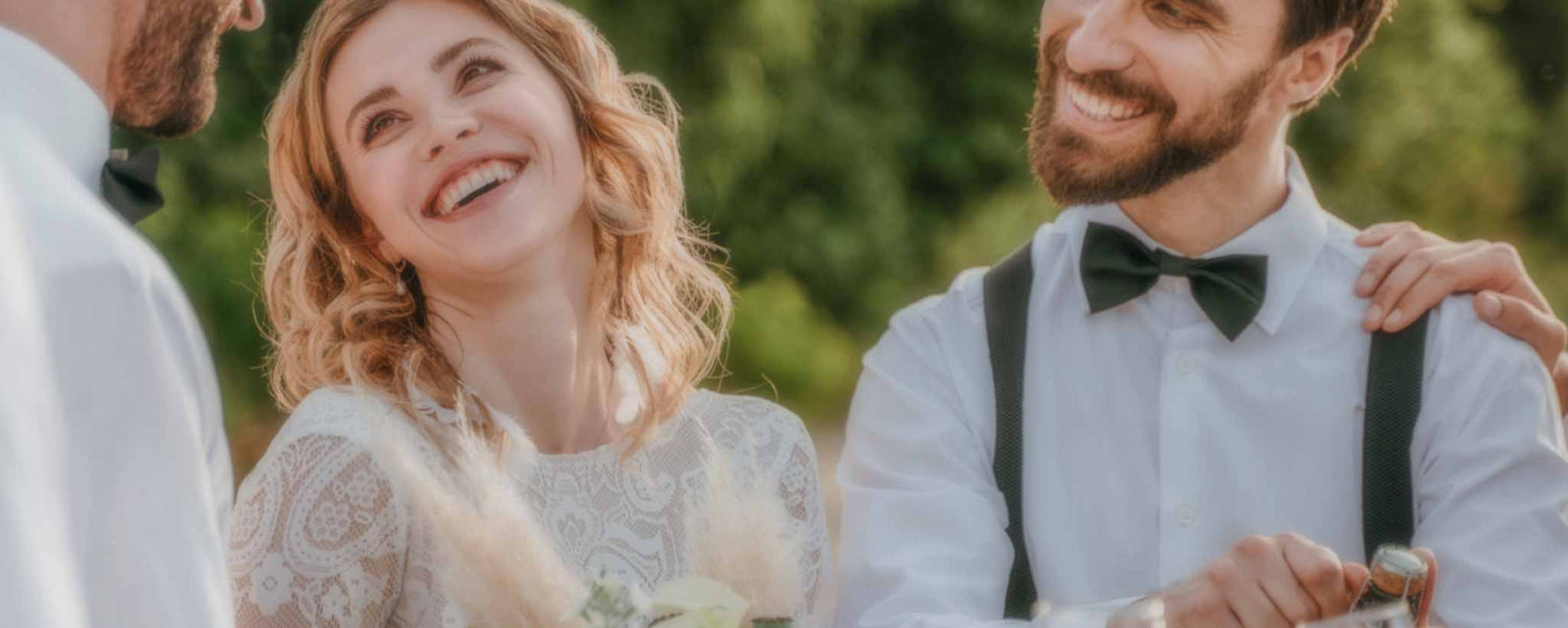 A happy wedding couple share champagne outdoors.