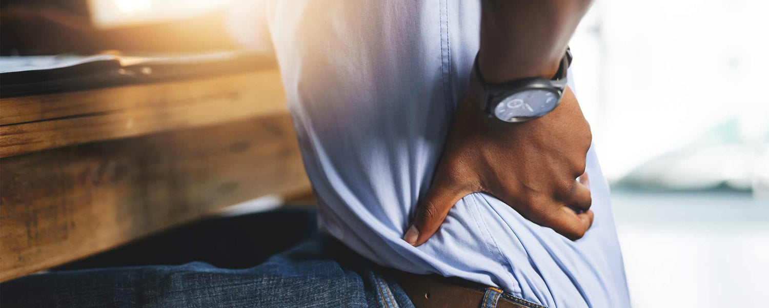 A seated man holding his back with a blurred background.