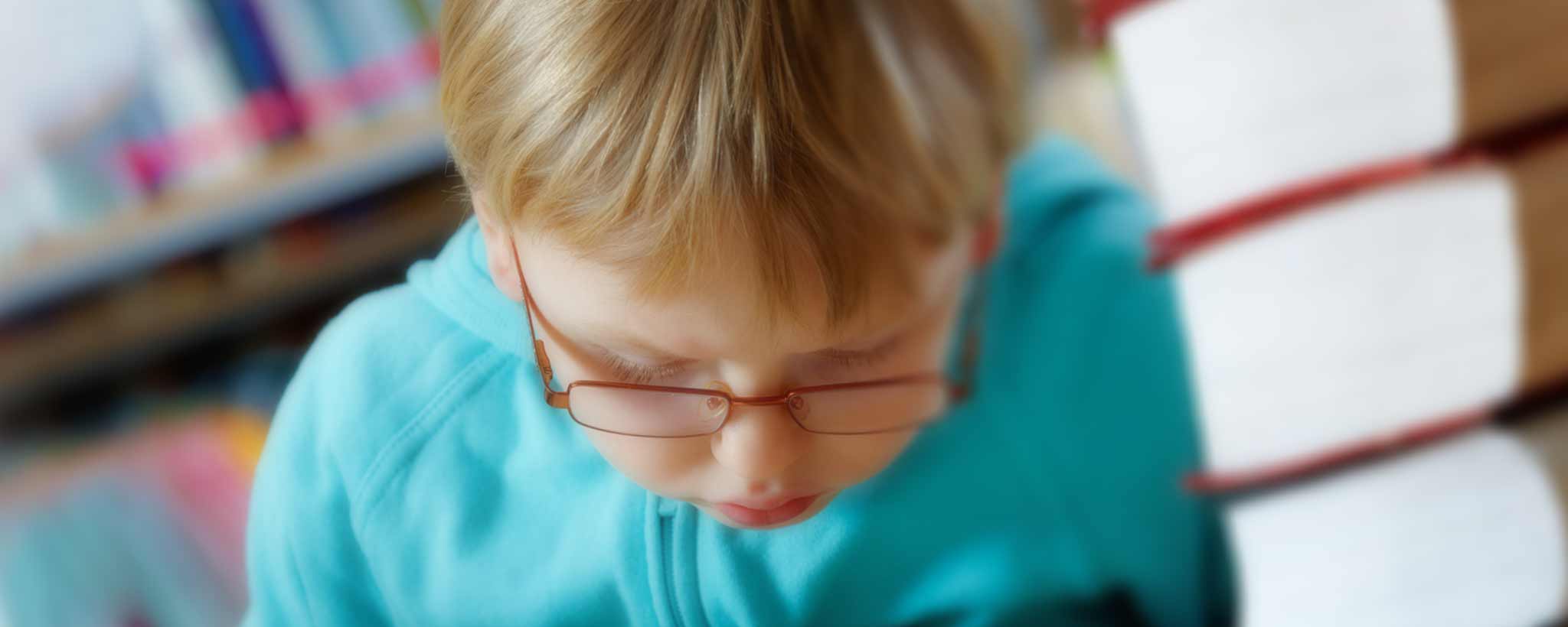 'Young boy reading next to stack of books'