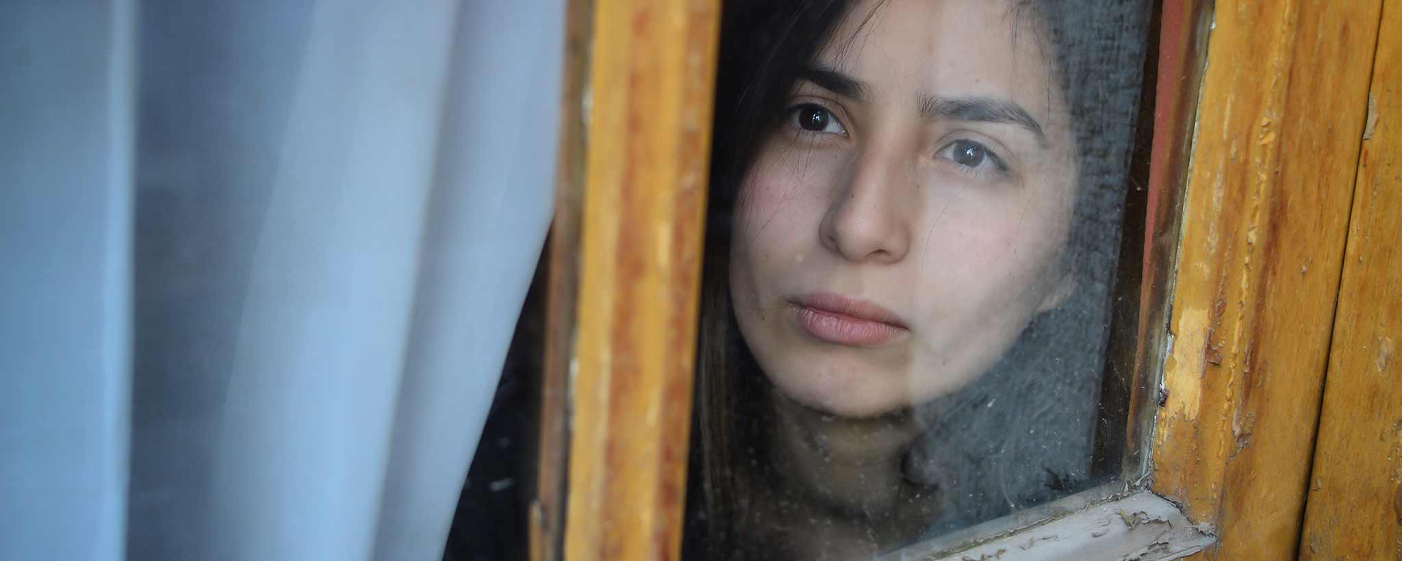 'A person looking out of a window with a wooden frame.'