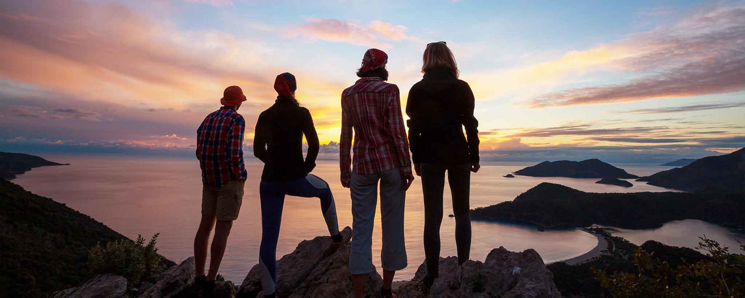 A silhouetted group of four people watch the sunset from a cliff.