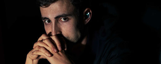 'A man sits in darkness, wearing a glowing earbud.'