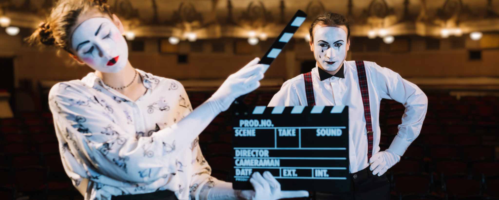 'Two mimes in a theater setting with one holding a clapperboard.'