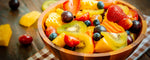 Wooden bowl filled with a colorful fruit salad on a checkered tablecloth.