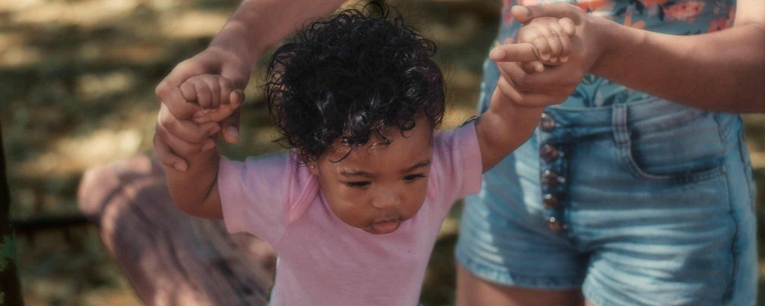 A mother helps her child walk at a park.
