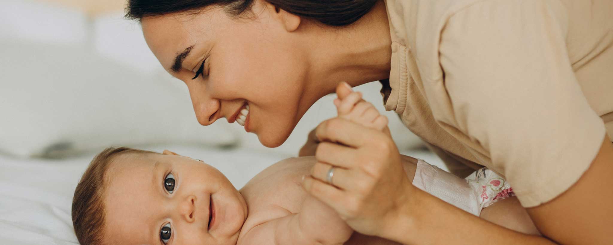 'A smiling mother leans over her baby, lying on the bed.'