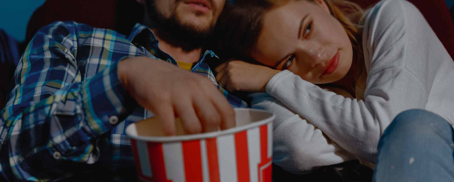 A man and young lady eat popcorn in a movie theater.