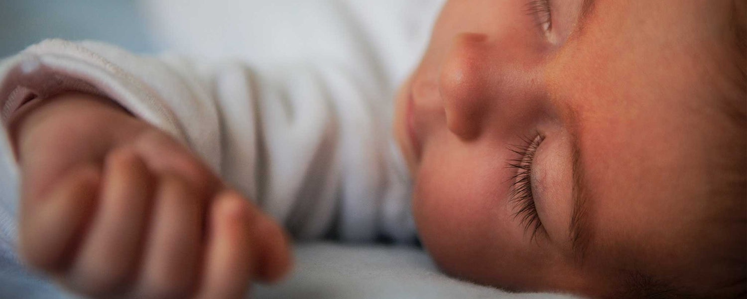 Close-up of a baby's face with closed eyes, wearing a white shirt.