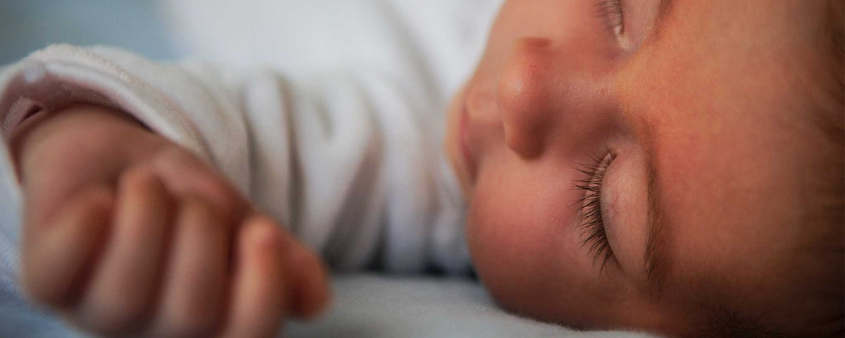 'Close-up of a baby's face with closed eyes, wearing a white shirt.'