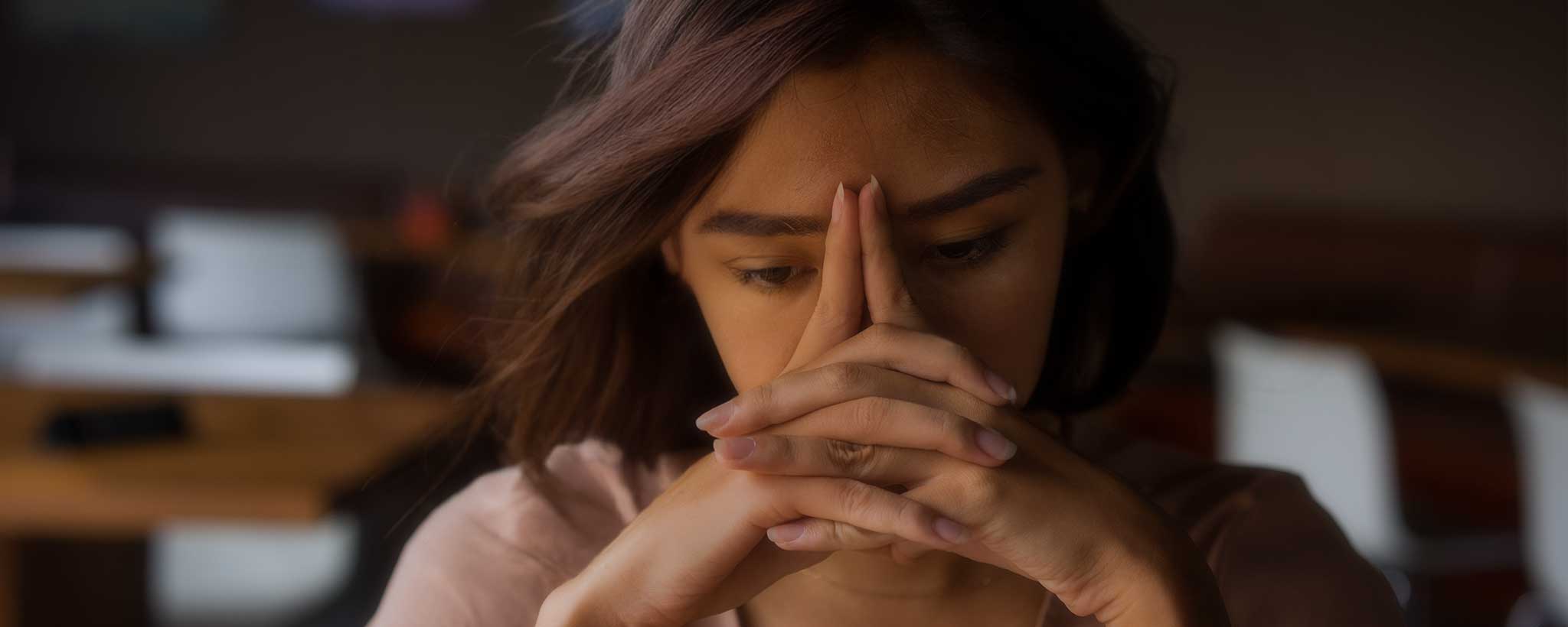 'A lady presses her fingers against her head during contemplation.'