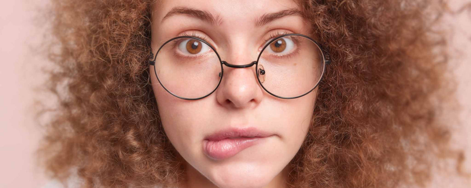 Close-up of a person with curly red hair and glasses biting her lip.