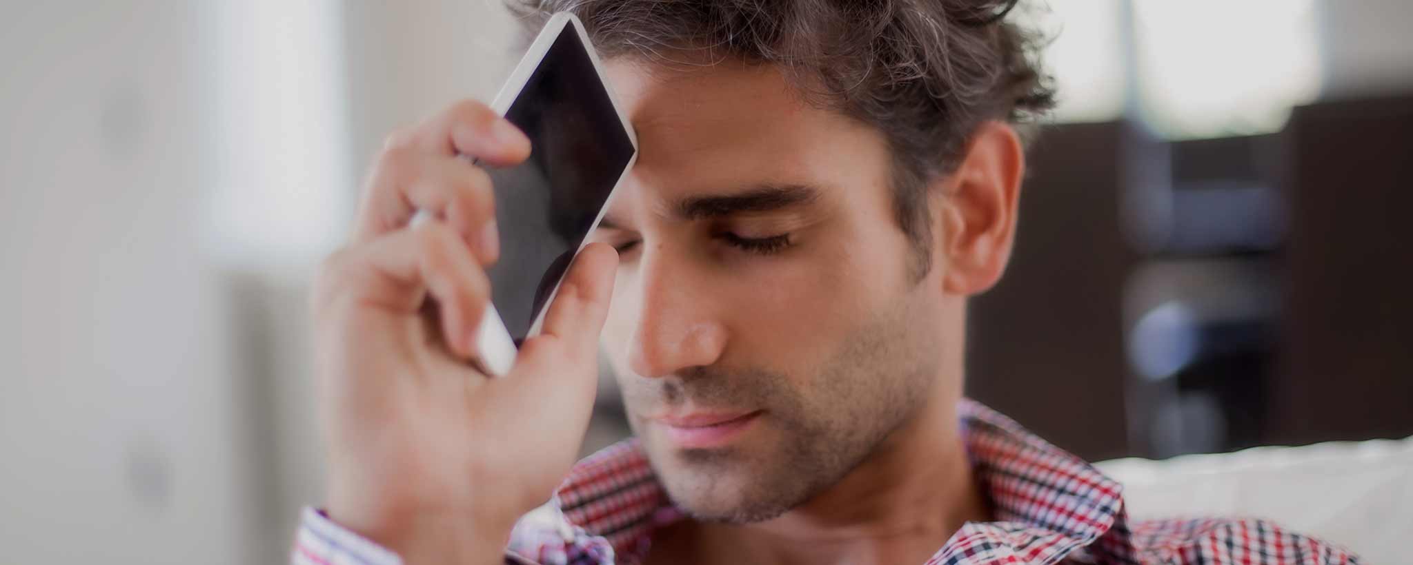 'A man holds his phone to his forehead.'