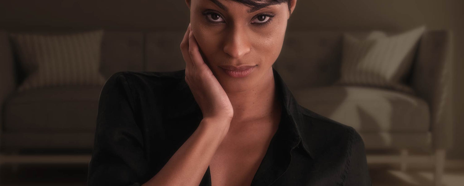 An alluring Black woman holds her hand on her cheek.