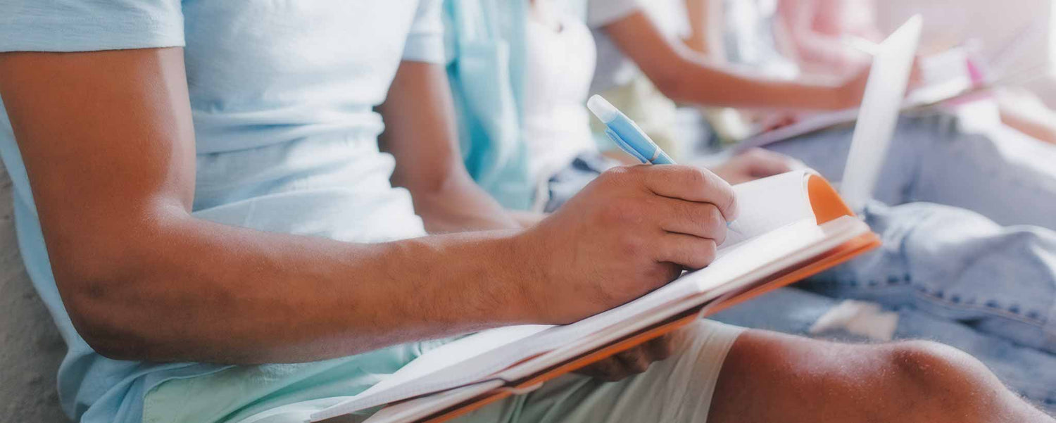A row of students writing on notebooks in their classroom.
