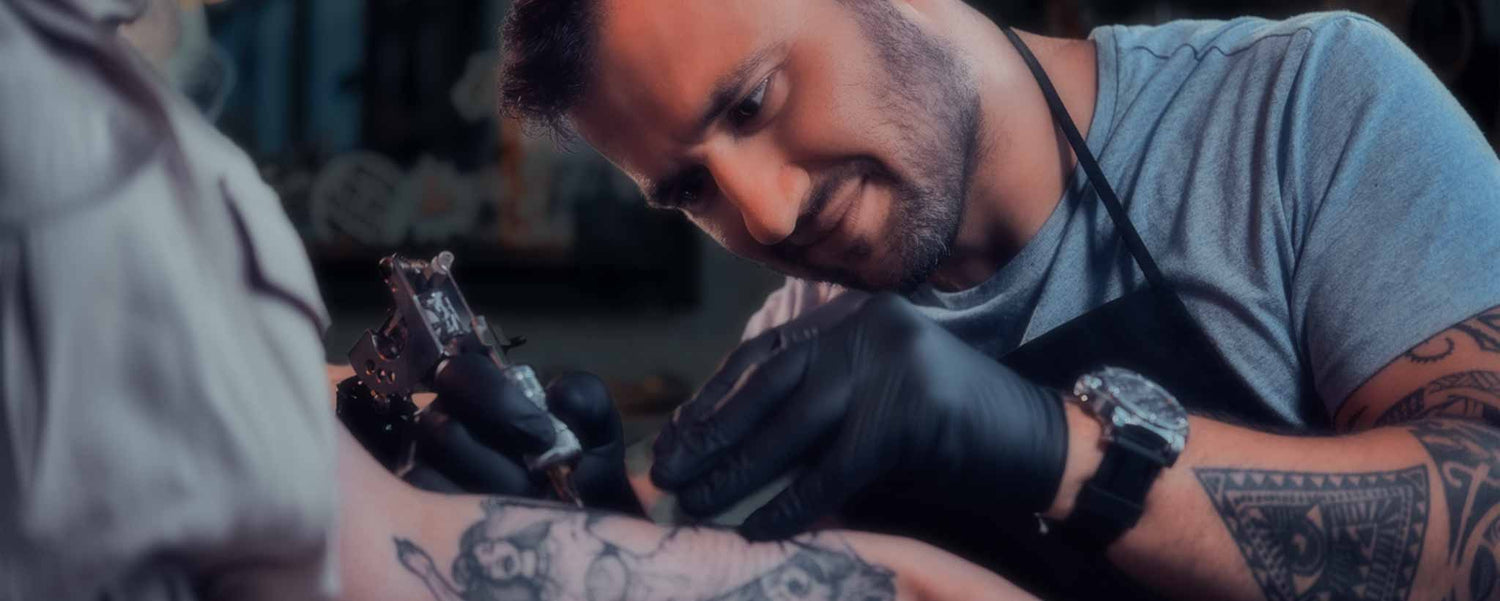 A tattoo artist inks a lady's arm.