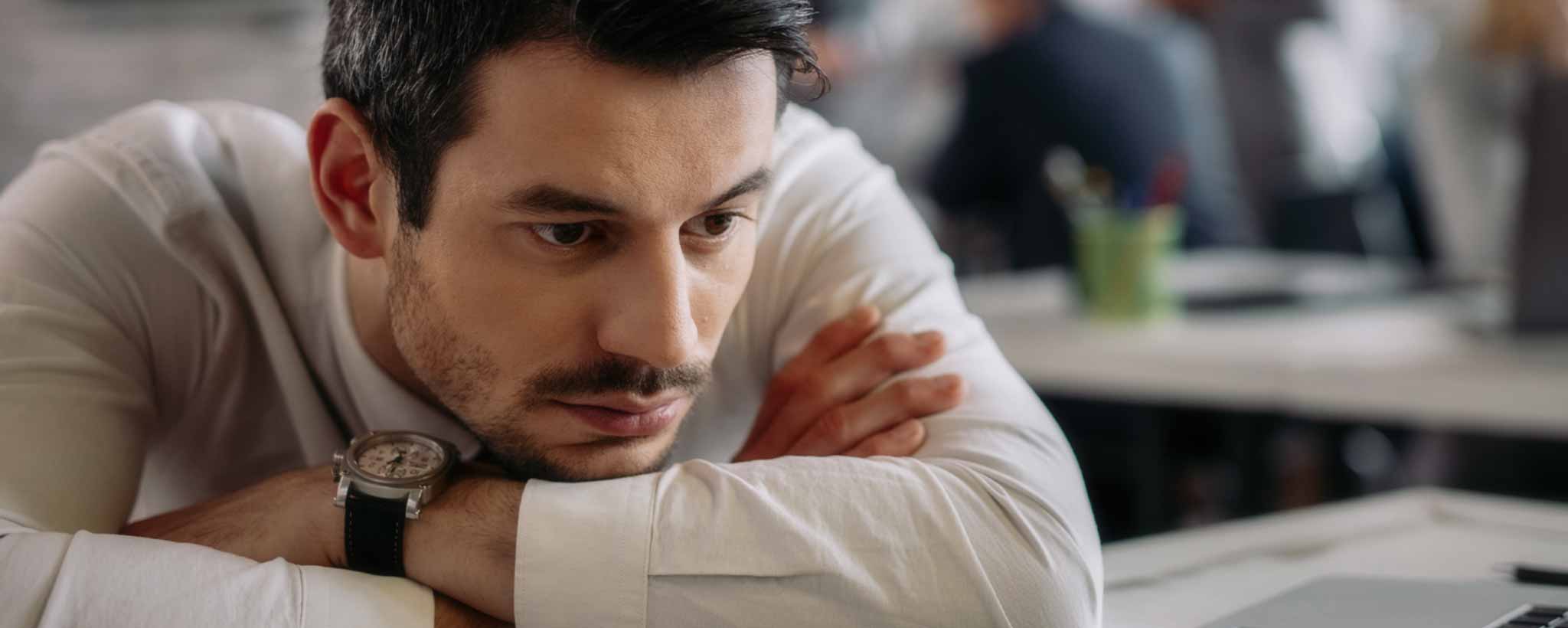 'Man at his office desk rests his head on his arms.'