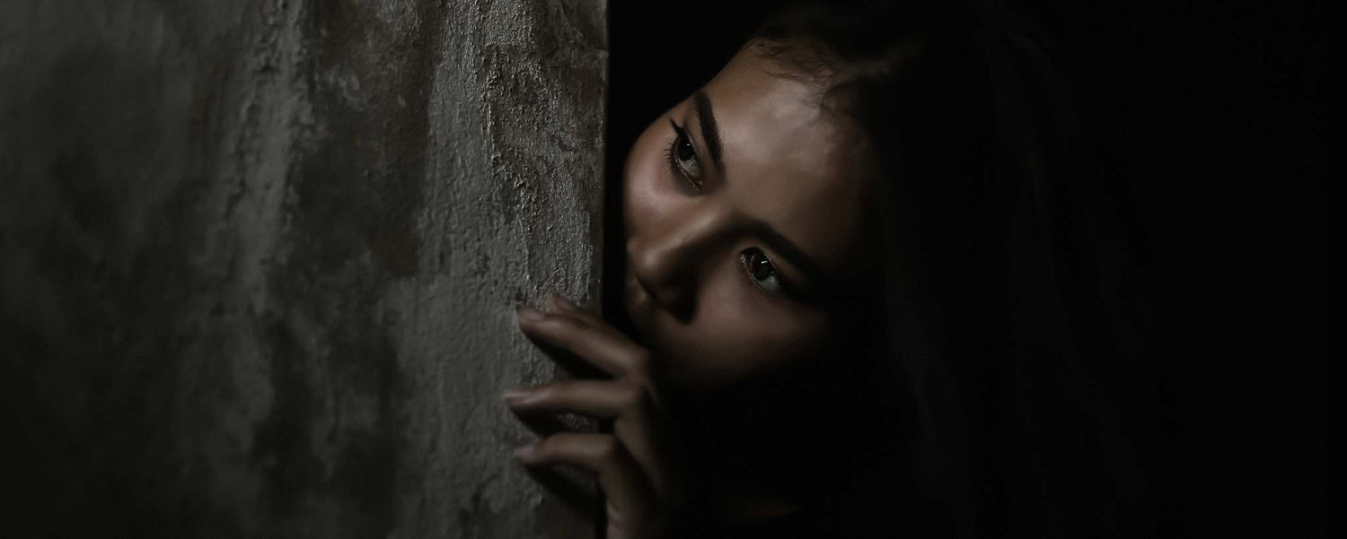 A female peers from around the corner in the darkness.