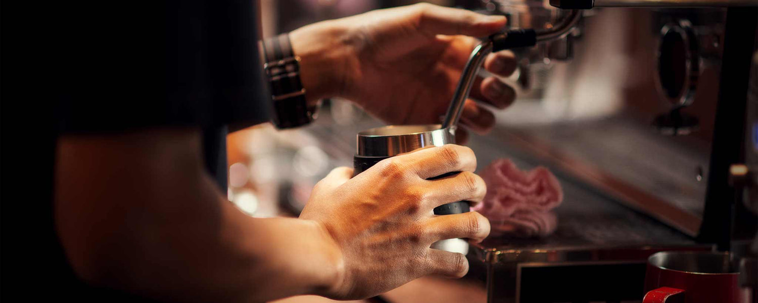 A barista's hands preparing a drink with a cappuccino machine.