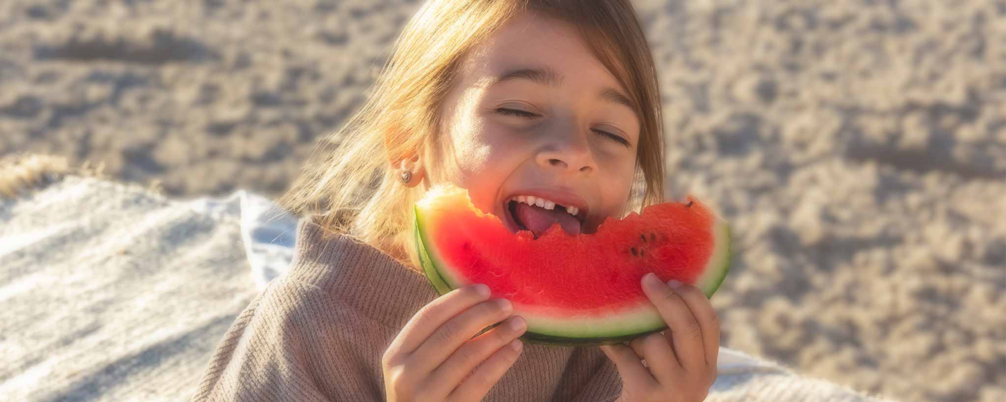'Blonde girl eating watermelon on beach to help maintain healthy body weight'