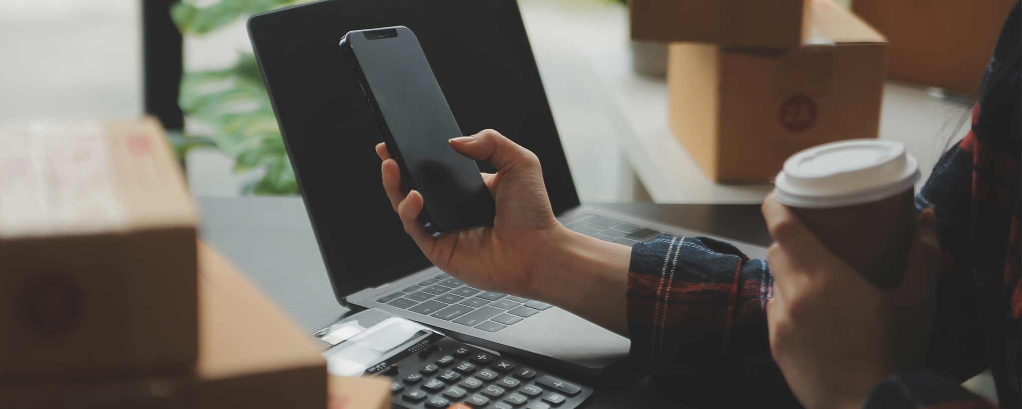 'Hand holding phone with boxes on a table'