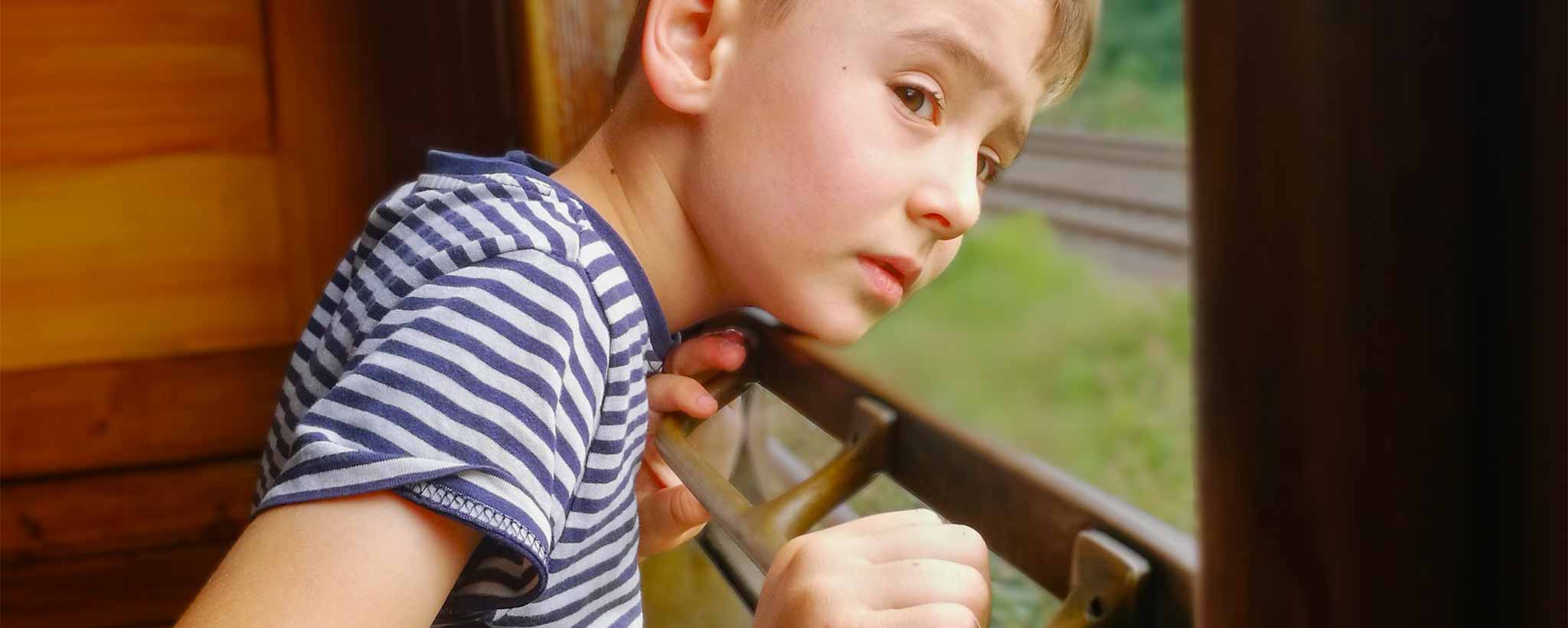 'A lonely child looking out of a window on a sunny day.'