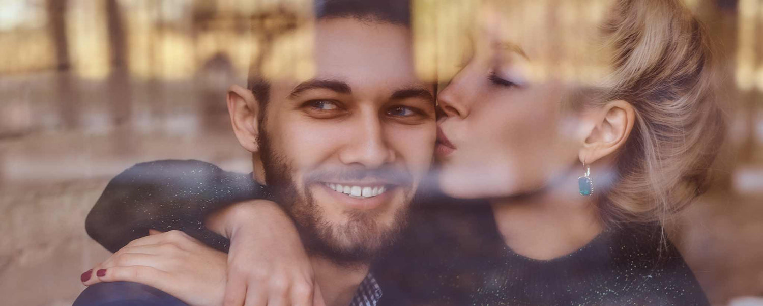 A couple in a café kiss with reflections on the window.