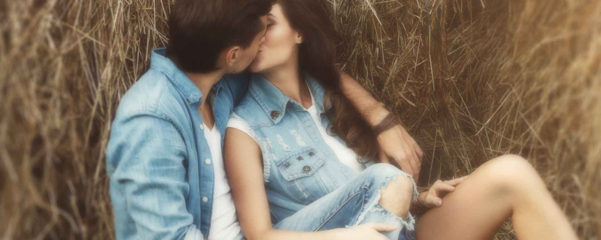 'A young couple kiss on a barn haystack.'