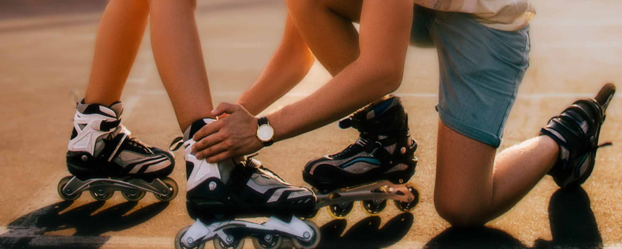 'A man straps rollerblade on a lady's foot. '