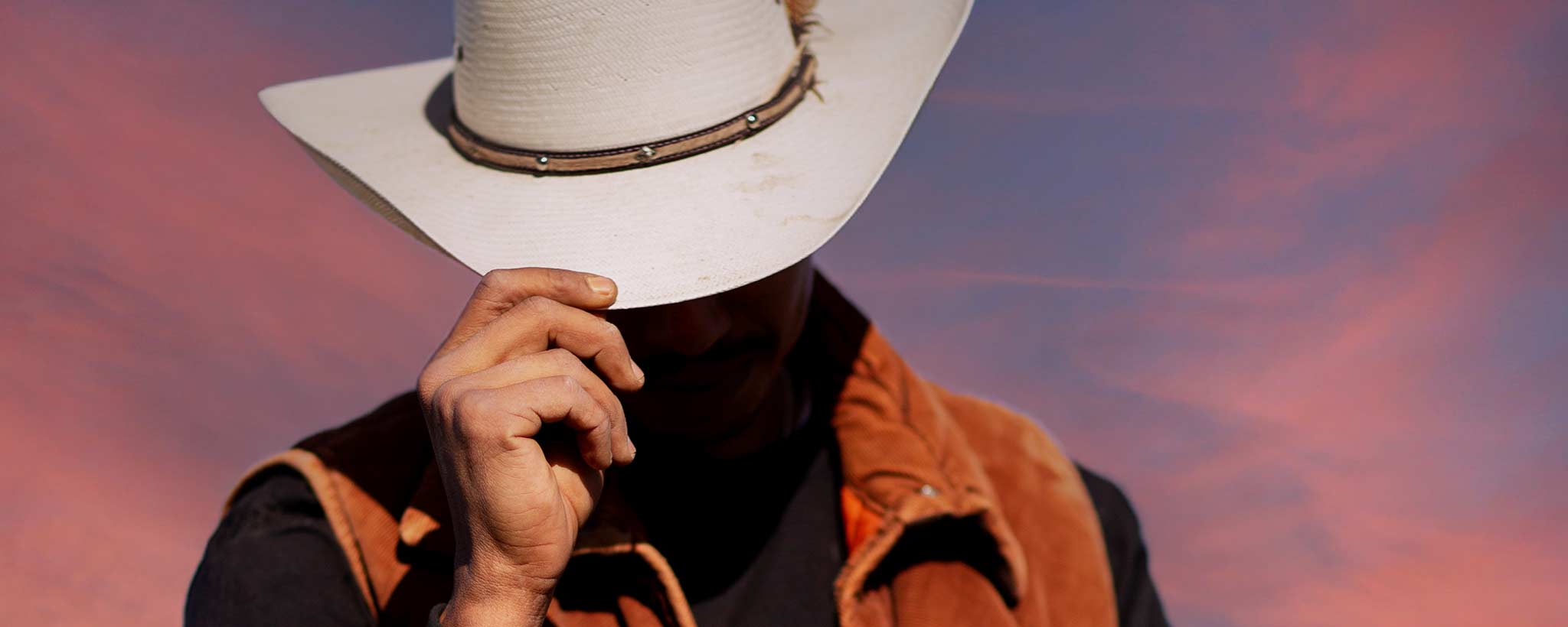 'A male cowboy with obscured face is tilting his hat.'