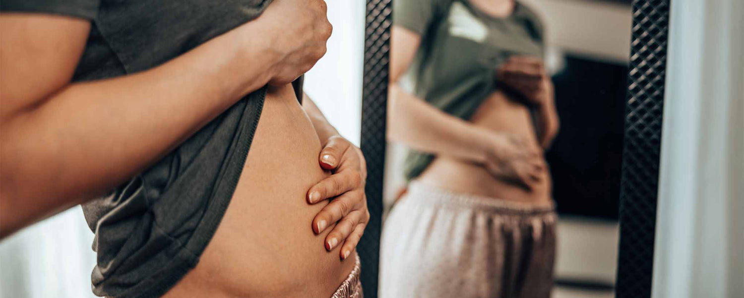 A lady looks in the mirror while rubbing her early-pregnancy belly.