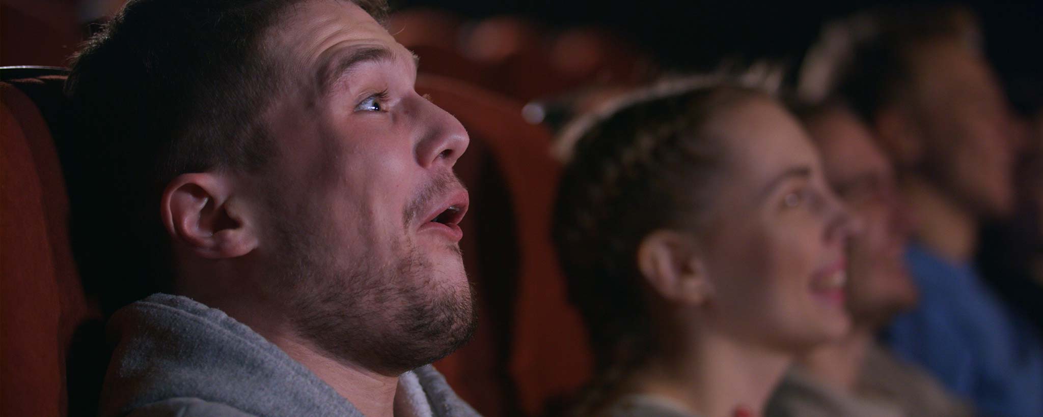 'People watching a movie in a theater with a focus on a man's surprised expression.'